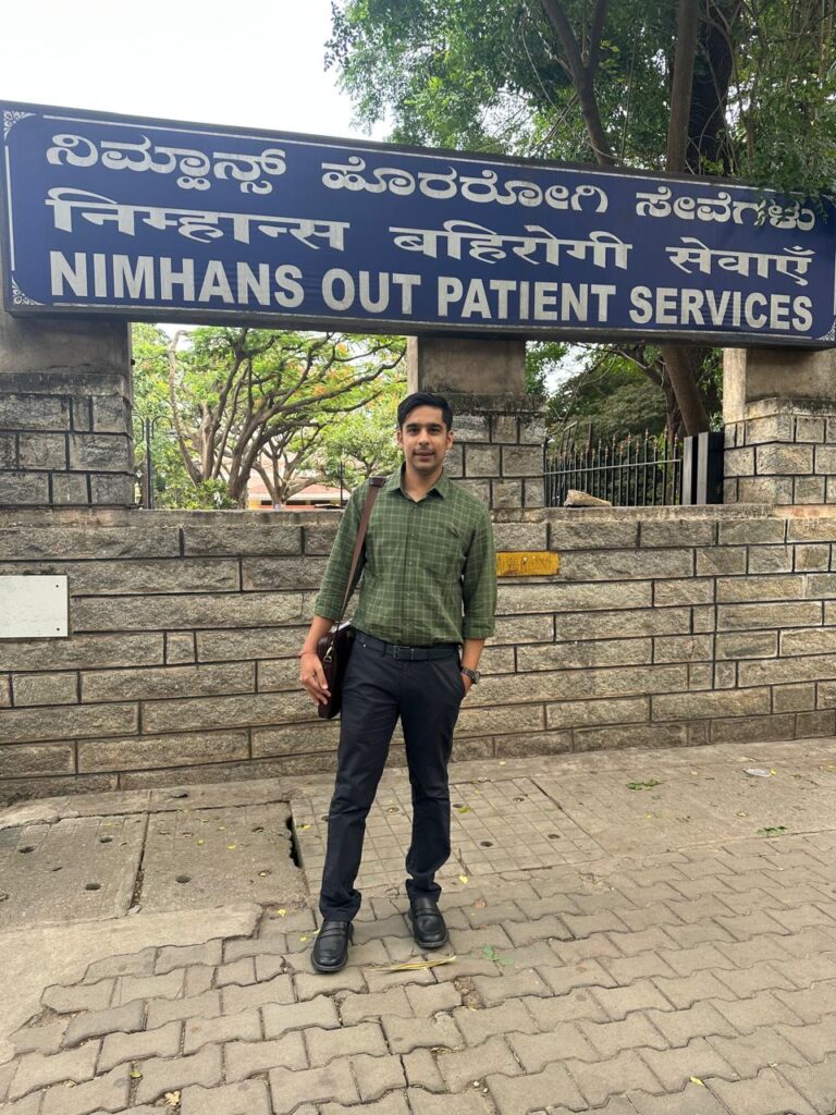 Dr Raghav Oza standing in front of the NIMHANS Out Patient Services signboard